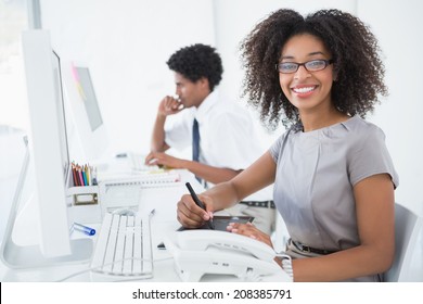 Young pretty designer smiling at camera at her desk in her office - Powered by Shutterstock