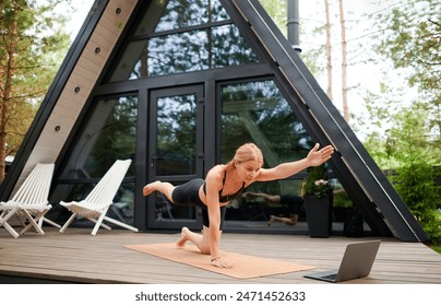 Young pretty European girl follows a workout with a video call coach on the terrace of her house during summertime, highlighting virtual training, outdoor fitness, summer exercise - Powered by Shutterstock