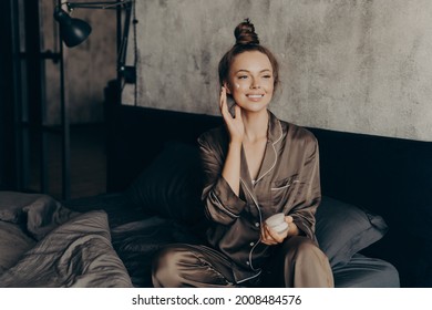 Young Pretty European Woman In Silk Pajama Takes Care Of Skin And Body After Waking Up In Morning At Home While Applying Moisturizing Face Cream, Getting Ready For Work. Beauty And Skincare Concept