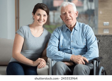Young pretty female caretaker and elderly man on a wheelchair