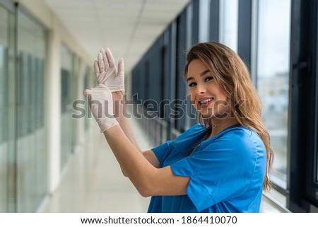 young pretty female doctor in blue uniform  wearing protective white gloves to prevent the spread of coronavirus