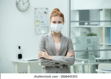 Young Pretty Female Manager In Suit And Protective Mask Crossing Arms By Chest While Standing In Office Environment In Front Of Camera