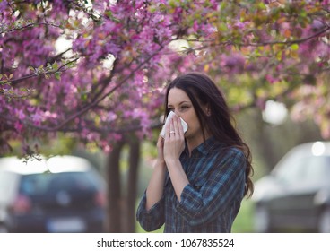Young pretty girl blowing nose in front of blooming tree. Spring allergy concept
