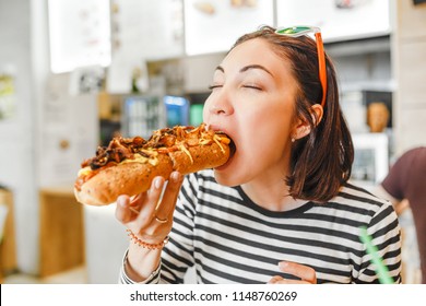 Young pretty girl eating big hotdog in fastfood restaurant