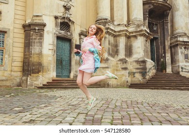 Young Pretty Girl With Extra Long Blonde Hair In Light Pink Dress And Knitted Sweater On The City Streets. Beautiful Fashion Woman Jumping Outdoors.