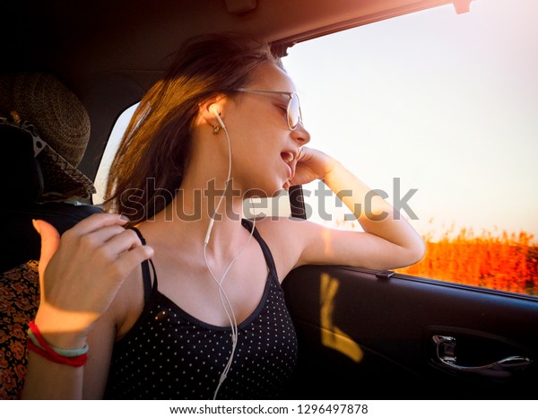 Young pretty girl in headphones listening to music\
and singing sitting in\
car