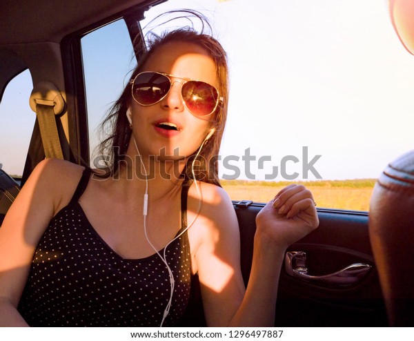 Young pretty girl in headphones listening to music
and singing sitting in
car