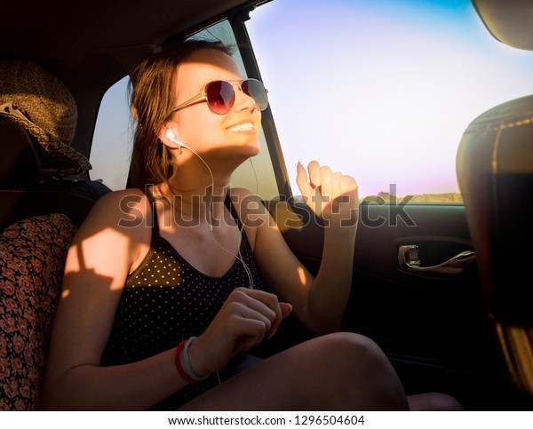 Young pretty girl in headphones listening to music\
and singing sitting in\
car