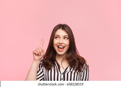 Young Pretty Girl Holding Finger Up Having Idea And Posing On Pink Background. 