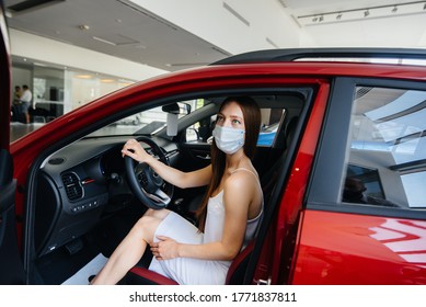 A Young Pretty Girl Inspects A New Car At A Car Dealership In A Mask During The Pandemic. The Sale And Purchase Of Cars, In The Period Of Pandemia.