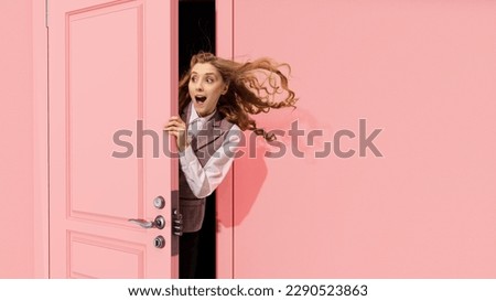 Young pretty girl peeking out open pink door and looking with positive excitement, astonishment. Surprised look. Good news, sales. Concept of emotions, facial expression, lifestyle