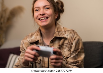 A young pretty girl plays a video game on a beige background. Close-up. The girl laughs, rejoices to win. Online games with friends, entertainment, win, prizes, surprises, virtual reality.
