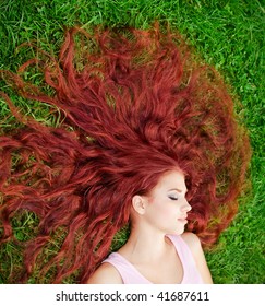 Young pretty girl with red hair lying on grass
