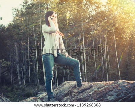 Young pretty girl smiles and talks on the phone while standing on a large stone
