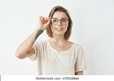 Young pretty girl smiling looking at camera correcting glasses over white background.
