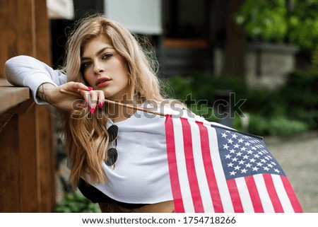 Young pretty girl in sunglasses stands on the street and holds an American flag in her hands. Independence Day