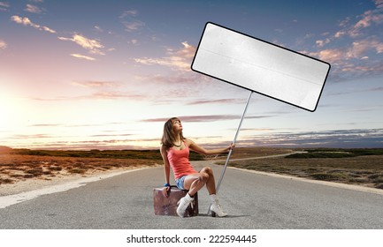 Young pretty girl traveler sitting on suitcase aside of road