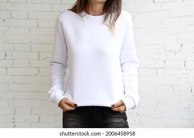 Young pretty girl wearing blank white sweatshirt with space for logo or design, mock-up of black women's sweatshirt, white stone wall in the background