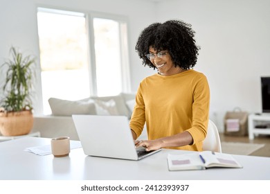 Young pretty happy smiling African American woman wearing eyeglasses using laptop computer sitting at home table hybrid working online, female student elearning, browsing web typing at pc. - Powered by Shutterstock