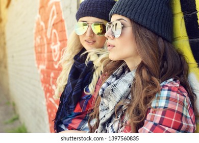 Young pretty hipster girls having fun outdoor, summer on the street. Teenage lifestyle. Trendy modern portrait of funny beautiful teen girls over grunge wall. Two young women have fun together 