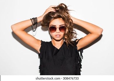 Young pretty hipster  woman in black trendy t-short and bikini  posing against white wall . Have perfect long wavy hairstyle wearing sunglasses .