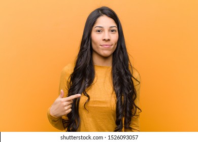 young pretty hispanic woman looking proud  confident   happy  smiling   pointing to self making number one sign against brown wall