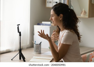 Young Pretty Hispanic Woman Sit At Desk Looking At Smartphone Camera Record New Educational, Entertaining Video Vlog. Online Counselling, Blogging, Videocall Event, Virtual Meeting, Streaming Concept