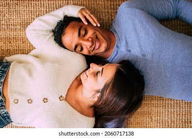 Young pretty interracial couple lay down on the carpet and smile having care and love of each other - happy and cheerful above portrait of boy and girl enjoying home together - concept life together