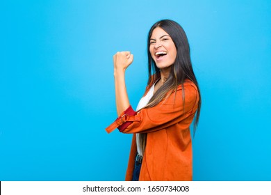 young pretty latin woman feeling happy, satisfied and powerful, flexing fit and muscular biceps, looking strong after the gym against flat wall - Shutterstock ID 1650734008