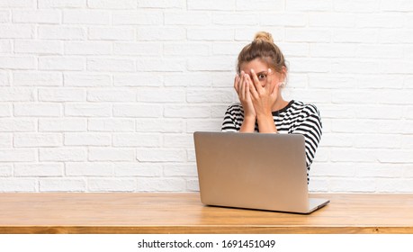 Young Pretty Latin Woman Feeling Scared Or Embarrassed, Peeking Or Spying With Eyes Half-covered With Hands Sitting With Her Laptop