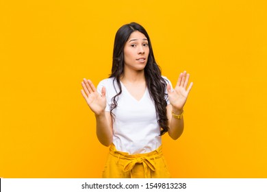 Young Pretty Latin Woman Looking Nervous, Anxious And Concerned, Saying Not My Fault Or I Didn't Do It Against Yellow Wall