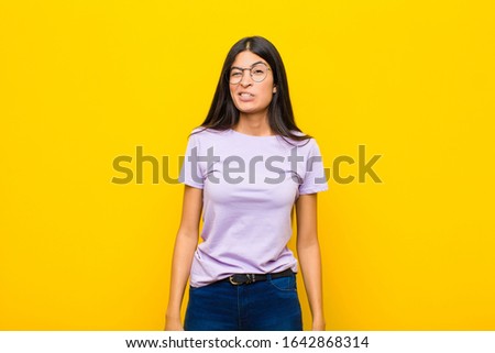 young pretty latin woman looking goofy and funny with a silly cross-eyed expression, joking and fooling around against flat wall