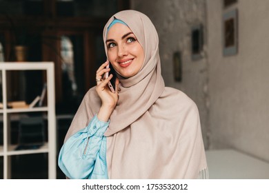 Young Pretty Modern Muslim Woman In Hijab Working On In Office Room, Education Online, Remote Work Freelancer, Talking On Smartphone