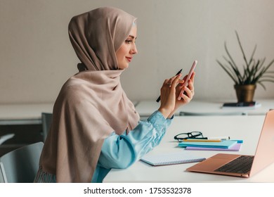 Young Pretty Modern Muslim Woman In Hijab Working On Laptop In Office Room, Education Online, Remote Work Freelancer, Using Smartphone