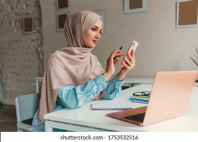 young pretty modern muslim woman in hijab working on laptop in office room, education online, remote work freelancer, using smartphone - Powered by Shutterstock