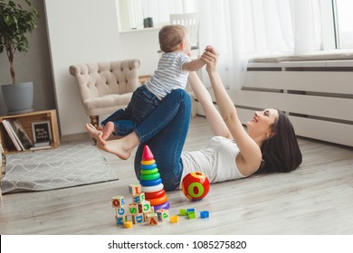 Young pretty mother playing with her little son. Cheerful family having fun indoors with little baby son