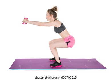 Young, Pretty Natural Looking Girl In Sport Bra And Pink Shorts Showing How To Do Proper Squat Exercise With Dumbbells On The Mat. Full Body Studio Shot, Pure White Background. 
