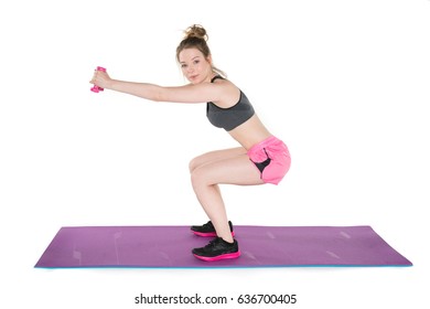 Young, Pretty Natural Looking Girl In Sport Bra And Pink Shorts Showing How To Do Proper Squat Exercise With Dumbbells On The Mat. Full Body Studio Shot, Pure White Background. 
