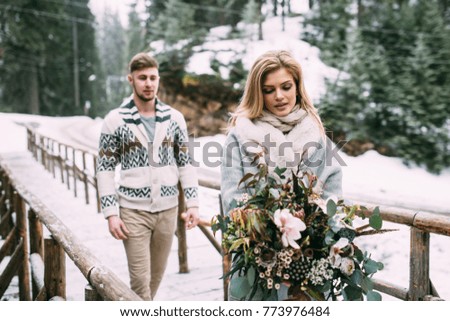Young pretty pair of lovers. Winter. Date. Man hugging woman on wooden bridge in mountain