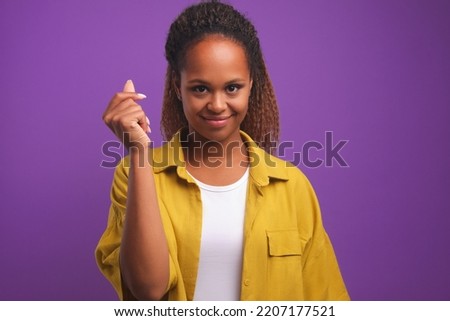 Young pretty positive African American woman with slight smile snaps finger demonstrating simplicity of some action or agreeing to bet with friends stands on plain purple background