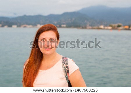 A young pretty redheaded woman standing on a background of sea