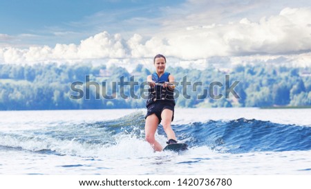 Young pretty slim brunette woman riding wakeboard on wave of motorboat in a summer lake