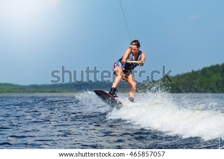 Young pretty slim brunette woman riding wakeboard on wave of motorboat in a summer lake