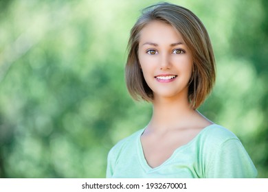 Junge schöne lächelnde Frau in einer grünen Bluse mit kurzen Haaren, Nahaufnahme im Sommerpark.