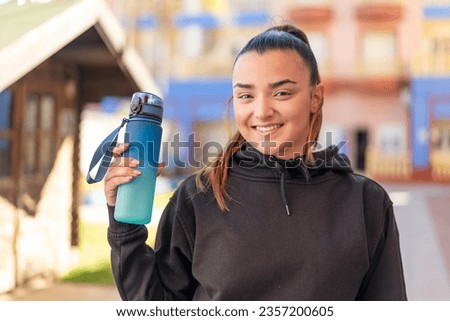 Young pretty sport woman with a bottle of water at outdoors smiling a lot