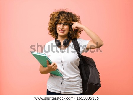 young pretty student woman feeling confused and puzzled, showing you are insane, crazy or out of your mind against pink wall
