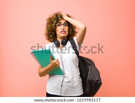 young pretty student woman raising palm to forehead thinking oops, after making a stupid mistake or remembering, feeling dumb against pink wall