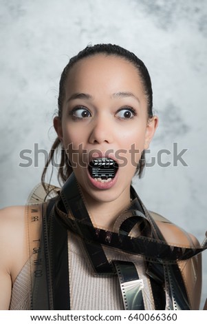 Young pretty teen woman funny face expression with little movie clapper board in her mouth and 35 mm filmstrip around body