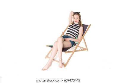 Young, Pretty Teenager Sitting On Sunbed Wearing Blue Shorts And Colorful Bikini Top. Studio Shot On Pure Isolated White Background