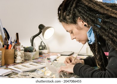 Young Pretty White Girl Hispanic Latin Art Director, With Dreadlocks And Good Style, In Her Artistic Production Studio, Tracing Onion Paper And With A Lot Of Work Tools On Her Well Lighted Work Table.